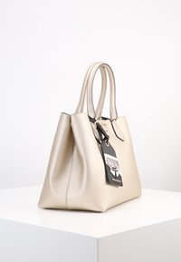 Gul läderhandväska med dubbla handtag, en strukturerad design och en svart etikett som visar en karaktär med glasögon och kostym.