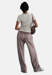 T-shirt aderente grigia chiara abbinata a pantaloni morbidi e larghi color taupe. L'outfit è completato da una piccola borsa marrone e sneakers grigie.