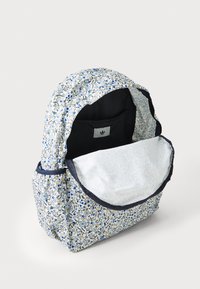 Rucksack mit Blumenmuster in Weiß, Blau und Gelb, mit einem dunkelblauen Rand, offenem oberen Teil und einem geräumigen Innenraum mit heller Fütterung.