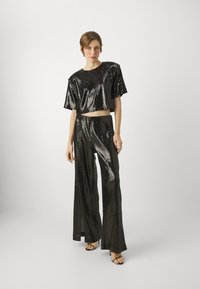 Svart paljett crop top og vide bukser-sett, med en skinnende finish og avslappet passform. Teksturen er glatt med reflekterende detaljer.