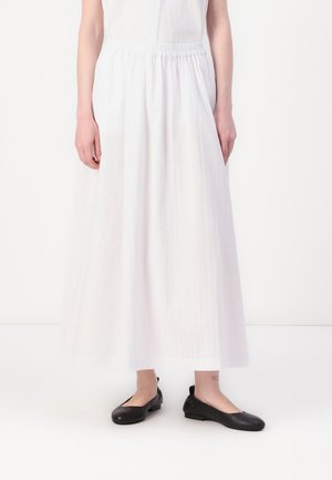 White ankle-length skirt made of lightweight fabric with an elastic waistband; paired with black flat shoes. Simple design, no patterns or accents.
