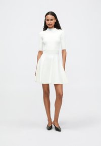 Vestido de patinadora blanco con un torso ajustado de canalé, mangas cortas y falda acampanada. Tejido suave y silueta sencilla sin estampados.