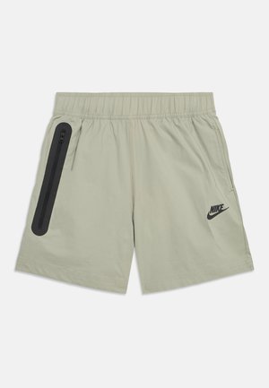 Shorts de sport Nike beige clair avec taille élastique, poche zippée verticale noire sur le côté gauche, et logo Nike noir sur la jambe droite.