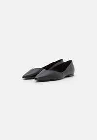 Scarpe basse in pelle nera con design a punta, texture liscia e stile minimalista. Tacco basso e piatto.