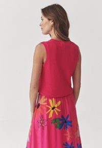 Top de punto sin mangas en un brillante color rosa, con un acabado texturizado. Combinado con una falda larga floral en colores y patrones vivos.