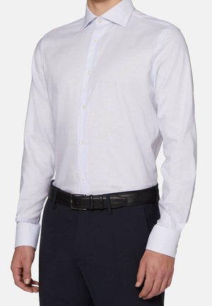 Hvid skjorte med lange ærmer og subtil tekstur, knappet foran, båret ned i mørke bukser med et sort læderbælte.