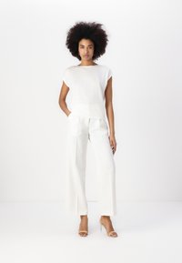 White textured short-sleeve top with a loose fit, paired with high-waisted, wide-leg white trousers and nude heeled sandals.