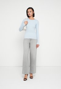 Svetlo modra majica z dolgimi rokavi, prilegajoča se v pasu, kombinirana z visokim pasom sivih širokih kavbojk in črnimi sandali z naramnicami. Bela torbica kot poudarek.