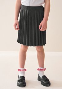 Grijze geplooide rok met een brede tailleband, gecombineerd met zwarte schoenen en witte sokken met rode gingham franjes.