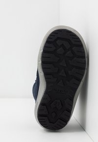 Zapato navy con un upper de tejido texturizado y una suela de goma negra que presenta un patrón de relieve geométrico. Acentos en gris en el borde de la suela.