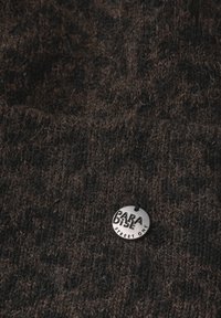 Tejido de punto marrón oscuro con un patrón texturizado y una etiqueta circular plateada inscrita con "PARADISE STREET ONE."