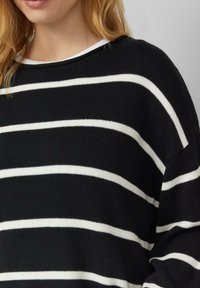 Czarnobiały sweter w paski wykonany na drutach o luźnym kroju i szerokim dekolcie, z wyraźnymi poziomymi paskami i teksturowaną tkaniną.
