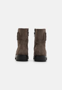 Botas de tobillo de ante marrón con un acabado suave, cremalleras laterales para facilitar el uso y suelas de goma negras, con acentos de hardware mínimos.