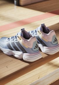 Scarpe da ginnastica azzurro chiaro con accenti grigi, tomaia in rete, colletto imbottito e suole bianche arrotondate. Presenta il logo Adidas sul tallone.