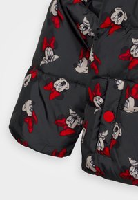 Sorte polstrede jakkeærme med rød knap og trykte gentagne Minnie Mouse-ansigtstræk med røde sløjfer.
