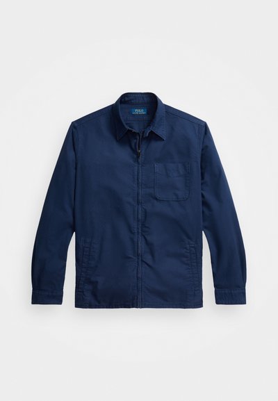 Chaqueta azul marino con cremallera, fabricada en tejido liviano. Presenta un cuello, mangas largas y un bolsillo en el pecho. Textura suave con un diseño minimalista.
