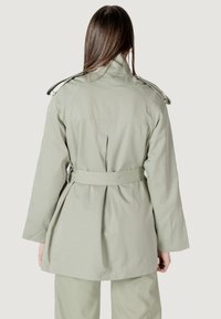 Trench coat verde chiaro con vita cintata, spalline e dettaglio in piega sul retro. Presenta un colletto classico e maniche lunghe.