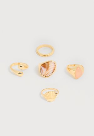 Cinq bagues en or avec des designs variés : une bague ouverte, une texturée, une avec un centre en coquillage, une avec une pierre rose, et une avec un détail en forme de coquillage.