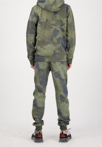 Camouflage hoodie og bukser i grønne og mørkegrå nuancer, med en afslappet pasform, blød tekstur og ribbede manchetter. Sorte sportssko.
