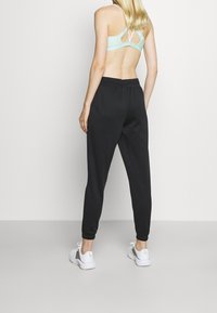 Pantalones de chándal negros con un corte holgado, que cuentan con un puño de canalé en los tobillos, combinados con un sujetador deportivo de color menta claro con tirantes entrecruzados.