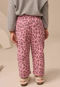Rosa leopardmönstrade byxor med resårmidja och bakfickor, i kombination med en grå långärmad topp och mjuka skor.