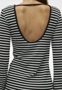 Haut à manches longues rayé avec un profond décolleté en V dans le dos, lignes horizontales noires et blanches, texture lisse avec un bord contrastant.