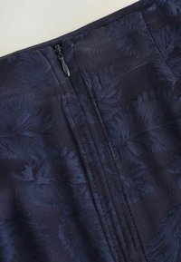 Gonna in tessuto blu scuro con una texture jacquard floreale, chiusura con zip sul retro e dettagli di cucitura pulita.