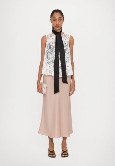 White lace sleeveless blouse with a black satin tie, paired with a blush pink midi skirt and black strappy sandals. Simple clutch in hand.