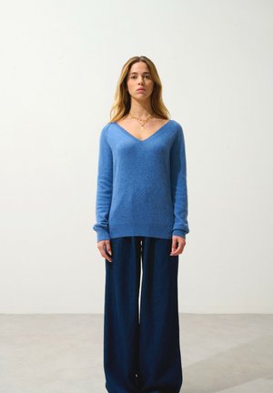 Pull bleu clair à col en V en maille douce, associé à un pantalon en denim foncé à jambes larges. Design simple avec manches longues et poignets côtelés.