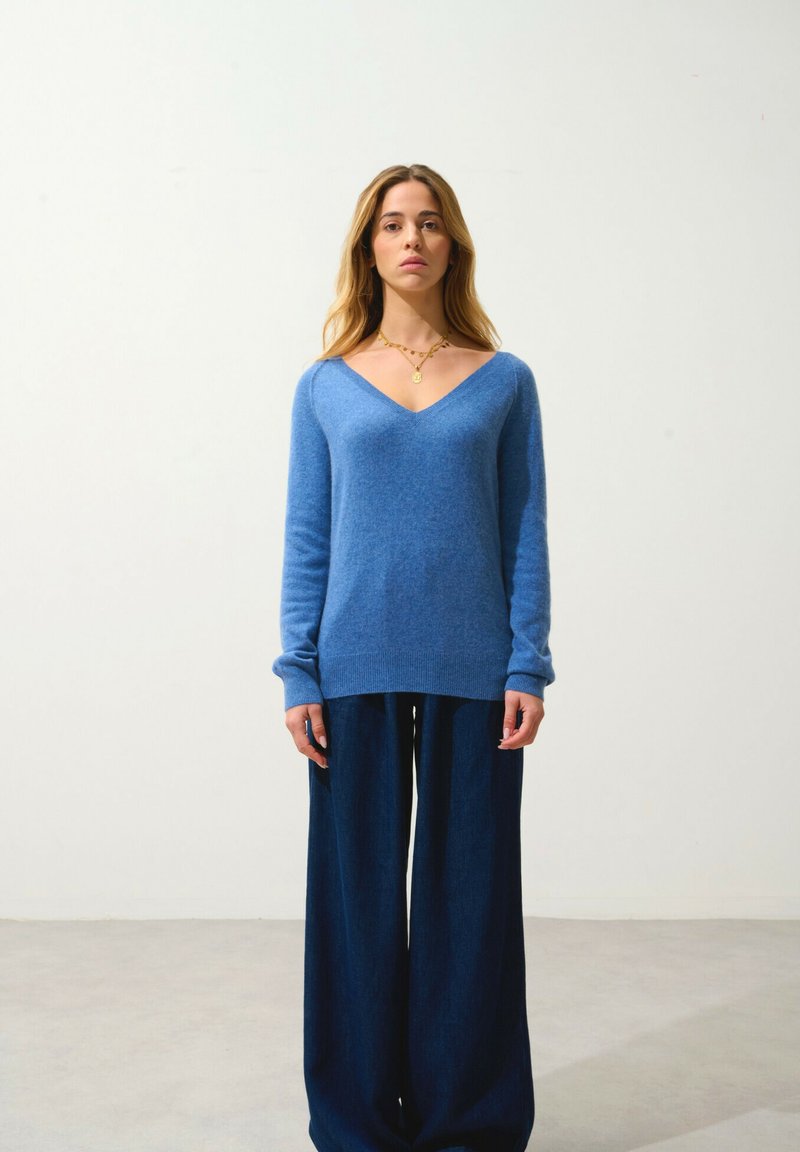Ljusblå V-ringad tröja i mjukt stickat material, i kombination med vida mörk denimbyxor. Enkelt mönster med långa ärmar och ribbade muddarna.