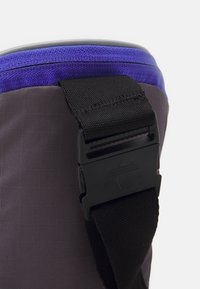 Gray fabric product with a textured surface, featuring a purple top band and a black plastic buckle on a nylon strap for fastening.