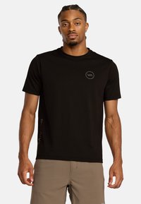 T-shirt nera a maniche corte realizzata in un materiale leggero, con un piccolo logo rotondo sul petto e un design testuale verticale sul lato.