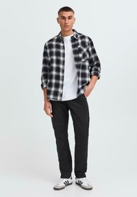 Koszula flanelowa w kratę w czerni i bieli z guzikami, noszona na białym T-shircie; połączona z wąskimi czarnymi spodniami i butami sportowymi.