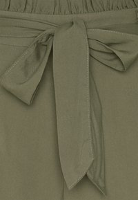 Olive green fabric with a textured waistband and a tied belt detail. The fabric appears smooth with neat stitching along the edges.