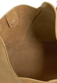 Interior of a tan suede bag showing stitched seams and a snap button closure on the inside flap.