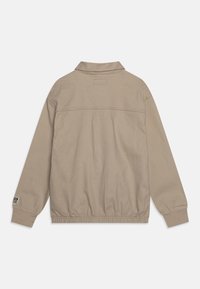 Beige lehká bunda s límcem, elastickým pasem a dlouhými rukávy. Disponuje hladkým povrchem a malým logem na manžetě.