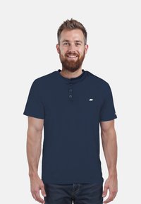 Navyblaues Baumwoll-T-Shirt mit kurzen Ärmeln, Knopfkraagen, geripptem Material und einem kleinen weißen Bärenlogo auf der Brust.