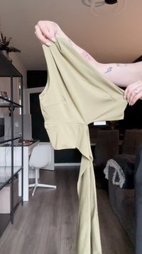 Olive green garment with a halter design, featuring two side pockets and a flowy, draped lower half. Made of smooth, lightweight fabric.