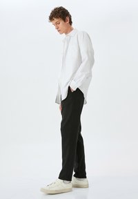 Witte lange mouw knopenhemd met een zak, gecombineerd met zwarte broeken en witte sneakers. Glad textuur, relaxte pasvorm.