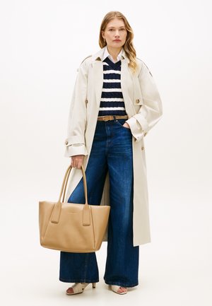 Borsa tote in pelle beige con doppi manici. Il modello indossa un trench color crema sopra un maglione a righe blu navy e bianco e jeans ampi a gamba larga.
