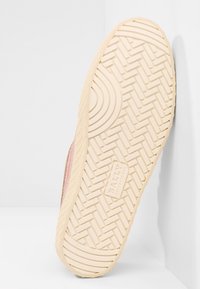 Semelle d'une basket beige avec un motif en arêtes de poisson et l'inscription "BALLY SWITZERLAND" embossée au centre, positionnée sur un fond blanc.