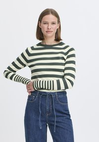 Top de manga larga a rayas en colores verde y crema, con mangas ajustadas, cuello redondo y textura acanalada. Combinado con jeans de tiro alto.