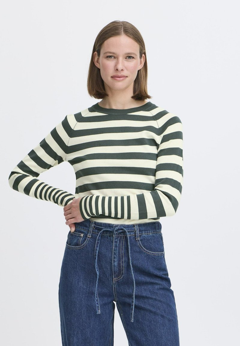Top de manga larga a rayas en colores verde y crema, con mangas ajustadas, cuello redondo y textura acanalada. Combinado con jeans de tiro alto.