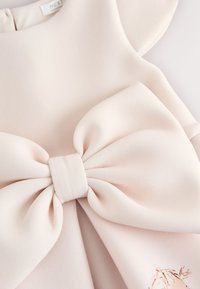 Blød lyserød stofkjole med en stor dekorativ sløjfe midt på brystet og subtile flæseærmer.