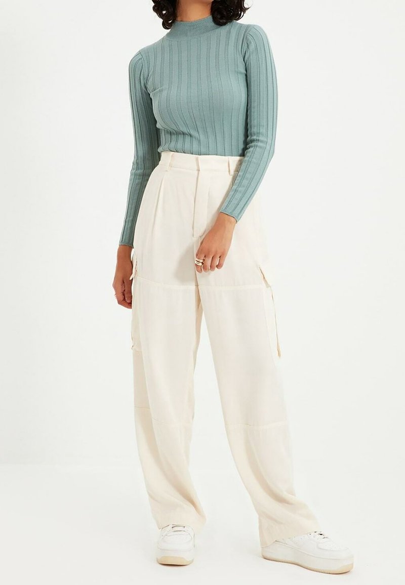 Jasnozielona, prążkowana bluzka z długim rękawem zestawiona z kremowymi spodniami w szerokim kroju z kieszeniami, dopełniona białymi trampkami.