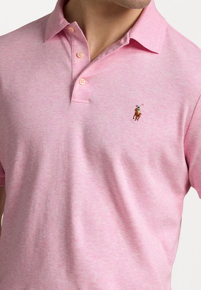 Polo de color rosa claro hecho de tela suave, con un cuello clásico y tres botones, y un pequeño logo bordado en el lado izquierdo del pecho.