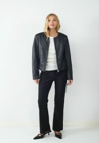 Czarna skórzana kurtka z okrągłym dekoltem, zapinana na zamek, w krótkim fasonie. Połączona z czarnymi spodniami i szpilkami z wydłużonym noskiem.