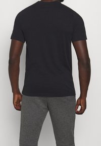 Camiseta negra de manga corta con escote redondo, hecha de algodón suave, vista desde la parte de atrás, combinada con pantalones de chándal grises.