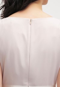 Robe rose pâle avec une finition satinée lisse, présentant un dos épuré et une fermeture éclair dissimulée au niveau de l'encolure.