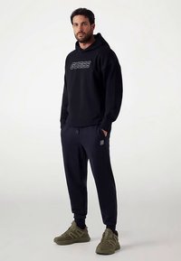 Must kapuutsiga pusa "GUESS" logoga, kombineeritud tume laevansiniste pükstega. Roheline oliivsest toonist spordijalatsid lõpetavad välimuse. Rõhk on mugavusel ja igapäevasel riietusel.